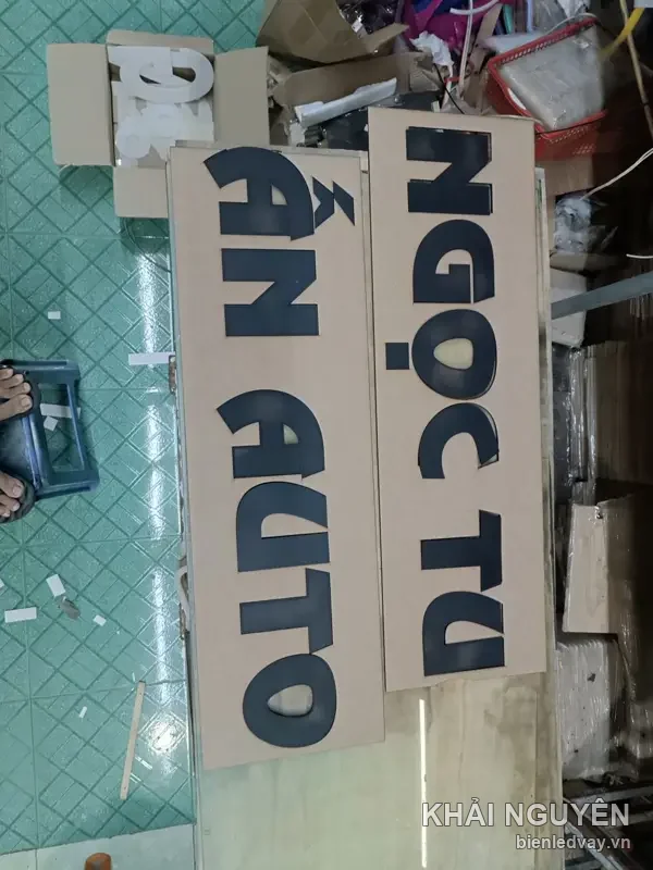 Chữ nổi mica đen Ngọc Tú và Ẩn Auto vừa cắt xong, xếp trên nền carton chờ lắp tại xưởng Khải Nguyên
