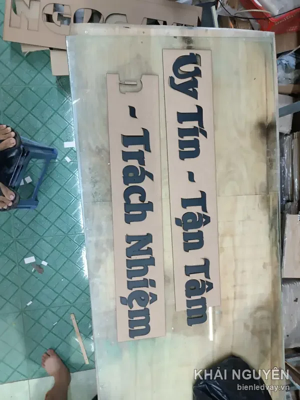 Chữ nổi mica đen dòng Uy Tín Tận Tâm và Trách Nhiệm, phôi chữ xếp trên tấm gỗ tại xưởng chờ ghép biển