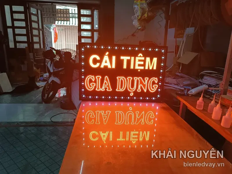 Biển vẫy LED chữ CÁI TIỆM vàng và GIA DỤNG cam, viền bóng LED trắng, hắt sáng xuống mặt bàn