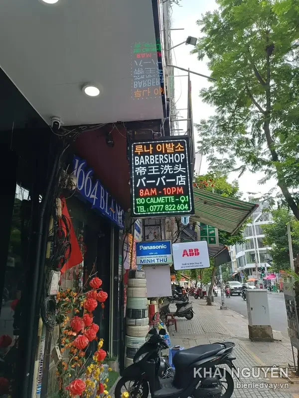 Hộp đèn barbershop treo dọc vỉa hè ghi BARBERSHOP kèm chữ Hàn và Nhật, giờ 8AM-10PM, 130 Calmette Q.1