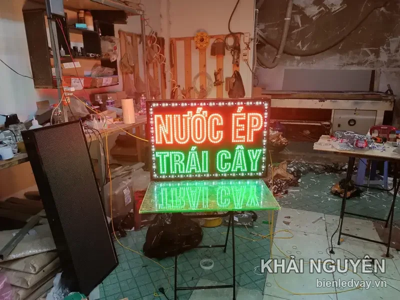 Biển LED chữ NƯỚC ÉP TRÁI CÂY đỏ và xanh, viền bóng trắng, đặt trên bàn tại xưởng