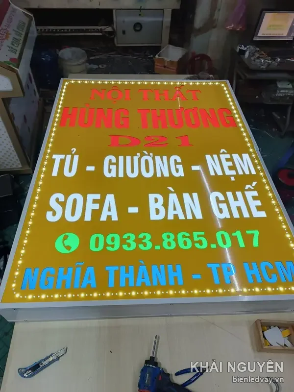 Cận cảnh hộp đèn vẫy NỘI THẤT HÙNG THƯƠNG D21 nền vàng, số liên hệ trên biển xanh lá, cạnh dao rọc và máy khoan