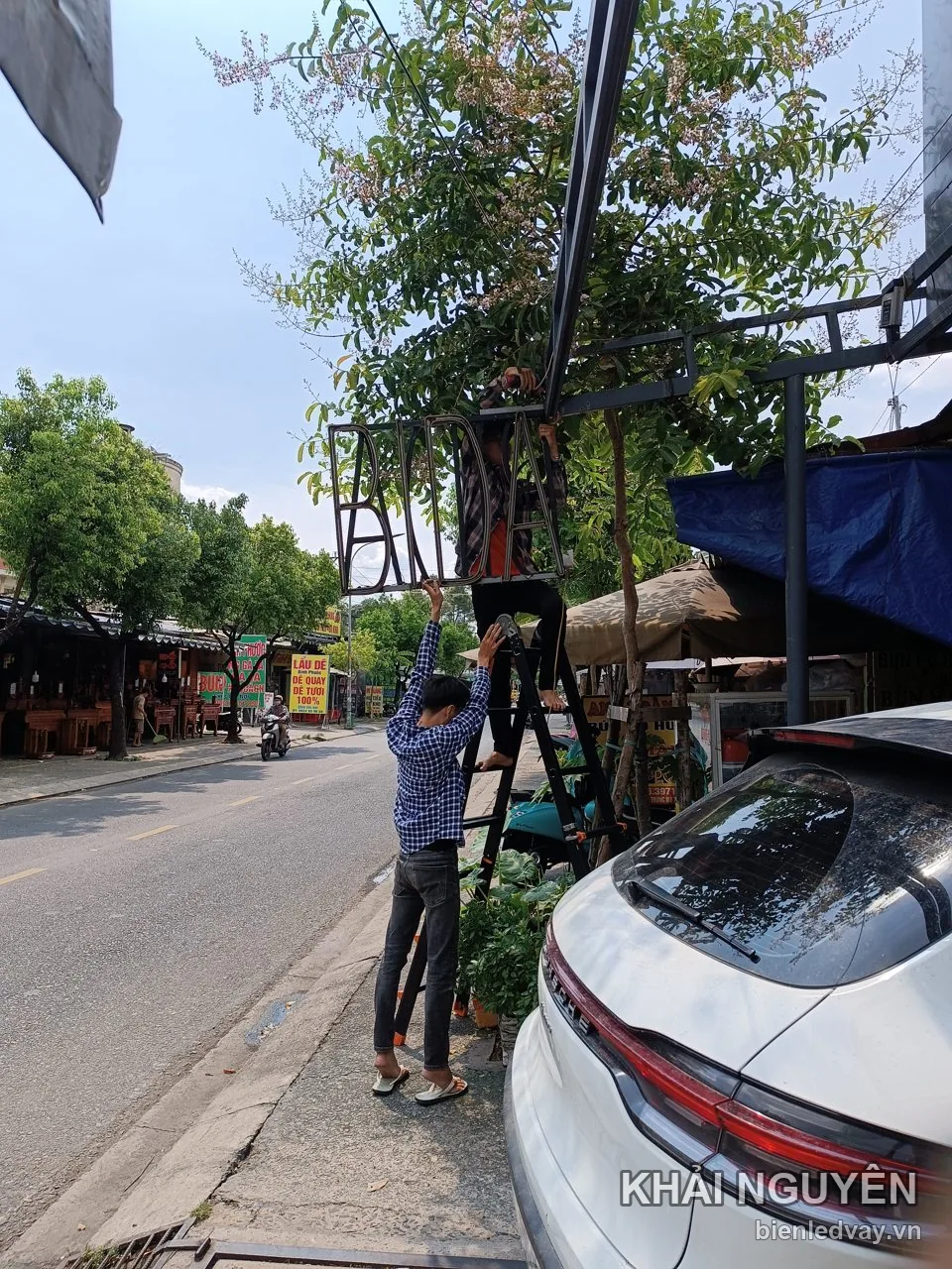 Thợ đứng thang lắp bộ chữ nổi BIDA lên khung sắt trước quán trên phố, ảnh chụp giữa trưa nắng