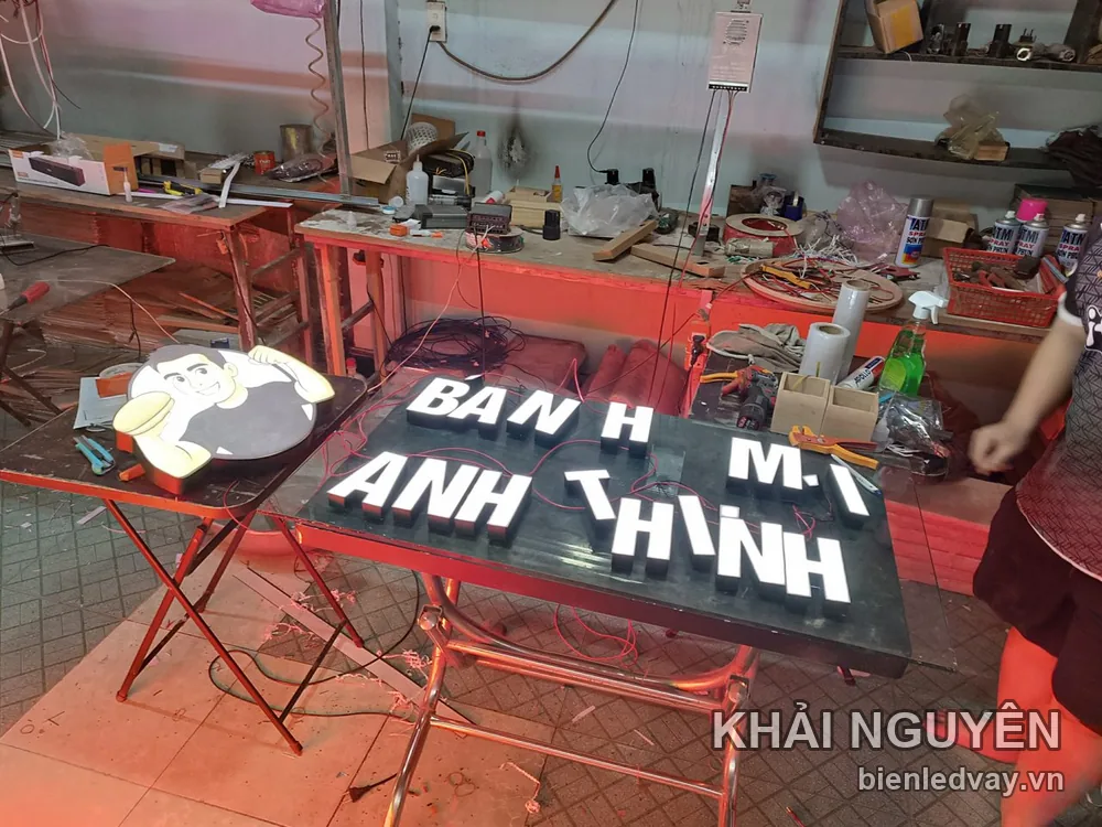 Chữ nổi mica trắng BÁNH MÌ ANH THỊNH trên nền đen, kèm mascot đầu bếp, đang lắp tại xưởng Khải Nguyên