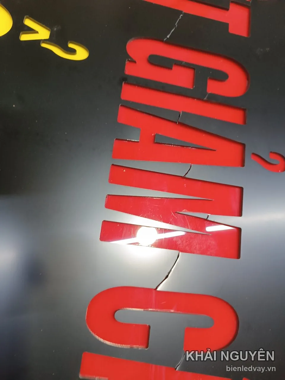 Cận cảnh chữ mica đỏ cắt CNC dán trên mặt biển đen bóng, đọc được chữ GIẢNG, cạnh đó có chữ mica vàng
