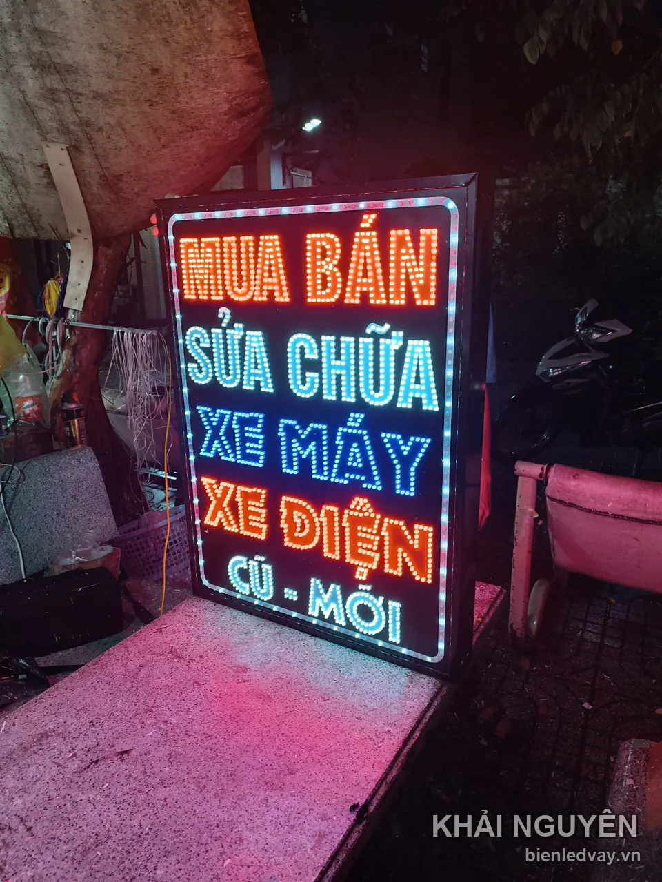 Biển vẫy sửa chữa xe máy và xe điện lắp ngoài tiệm vào ban đêm